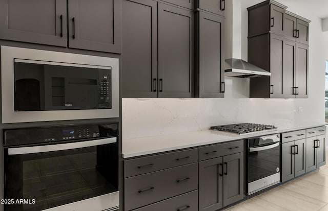 kitchen with gray cabinetry, light countertops, appliances with stainless steel finishes, wall chimney range hood, and backsplash