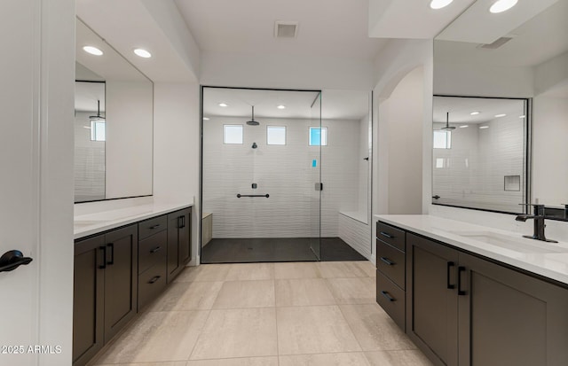 bathroom featuring recessed lighting, two vanities, a sink, and a tile shower