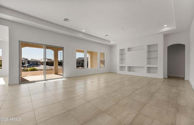 unfurnished living room featuring built in shelves, arched walkways, visible vents, and baseboards