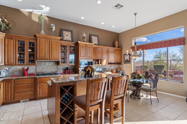 kitchen with appliances with stainless steel finishes, stone countertops, a kitchen breakfast bar, hanging light fixtures, and a kitchen island with sink