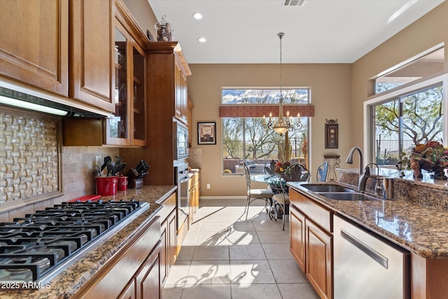 kitchen featuring sink, dark stone countertops, stainless steel appliances, decorative backsplash, and decorative light fixtures