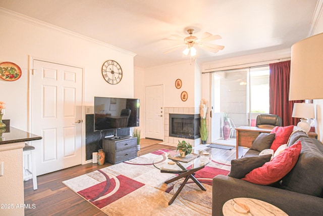 living area with wood finished floors, ceiling fan, a fireplace, and ornamental molding
