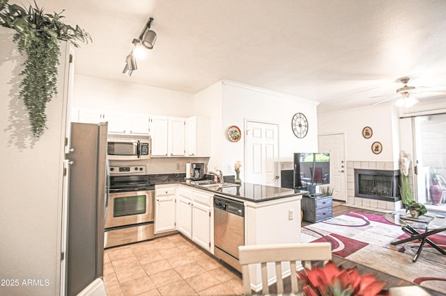 kitchen with a peninsula, appliances with stainless steel finishes, a sink, dark countertops, and a tiled fireplace