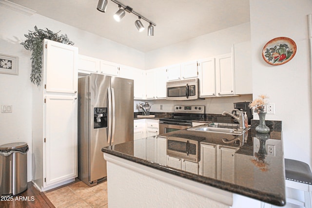 kitchen with a peninsula, white cabinets, dark stone counters, appliances with stainless steel finishes, and a sink