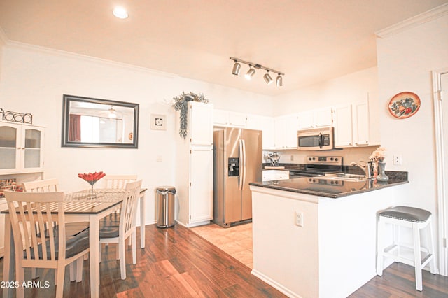 kitchen with a peninsula, white cabinetry, dark countertops, appliances with stainless steel finishes, and a sink