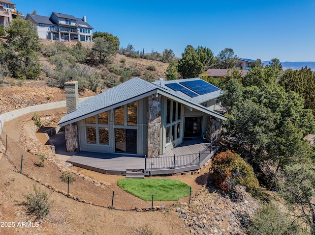 rear view of house featuring a deck, solar panels, stone siding, and a chimney