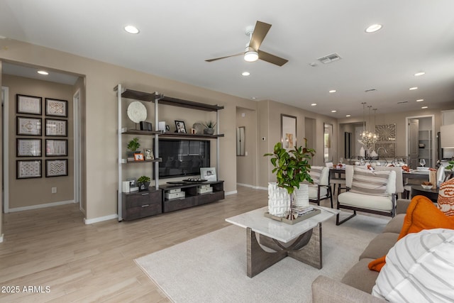 living area with light wood-type flooring, visible vents, baseboards, and ceiling fan with notable chandelier