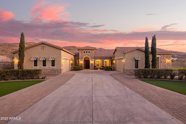 mediterranean / spanish house with stone siding, stucco siding, decorative driveway, and a garage