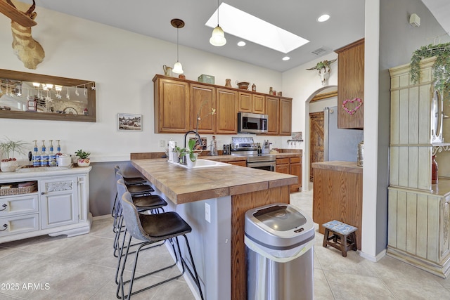 kitchen with a breakfast bar area, a skylight, a sink, appliances with stainless steel finishes, and brown cabinets