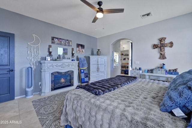 tiled bedroom featuring arched walkways, visible vents, a glass covered fireplace, and ceiling fan