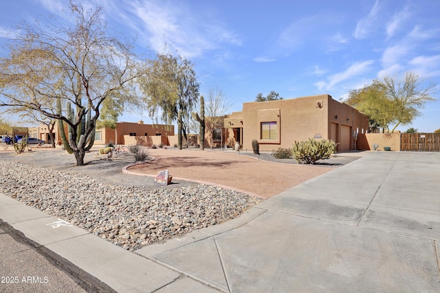 pueblo-style home featuring concrete driveway, fence, an attached garage, and stucco siding