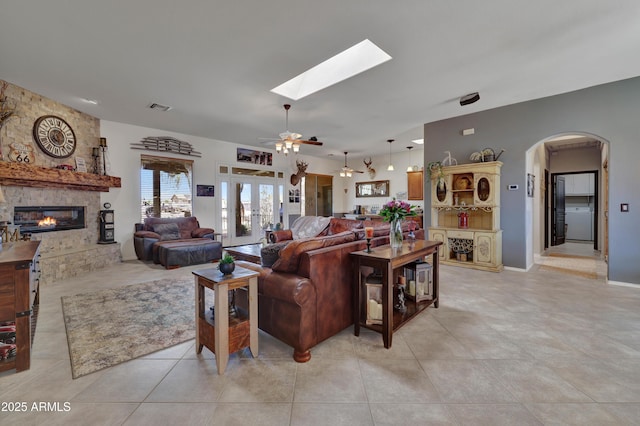 living room with a skylight, light tile patterned floors, visible vents, arched walkways, and a fireplace