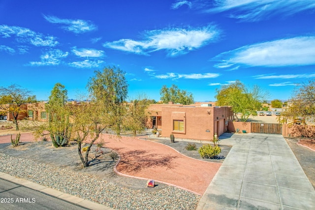 pueblo-style home with driveway, a chimney, fence, and stucco siding