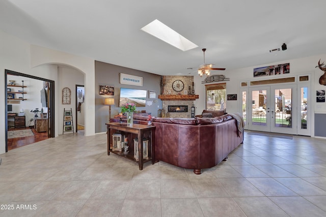 living area with light tile patterned floors, ceiling fan, a large fireplace, a skylight, and french doors