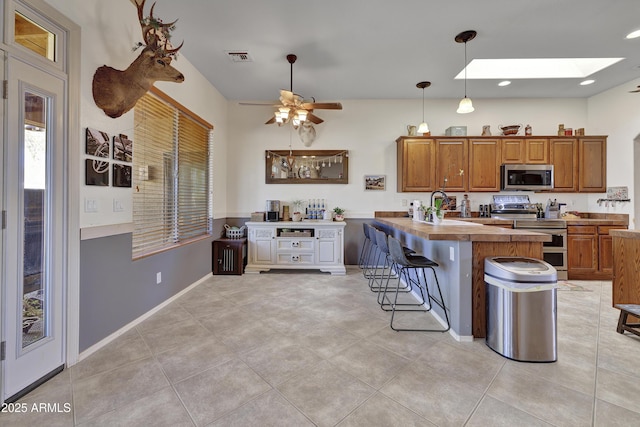 kitchen with a skylight, brown cabinetry, a peninsula, stainless steel appliances, and a kitchen bar