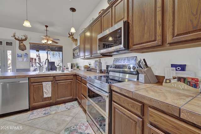 kitchen featuring stainless steel appliances, brown cabinetry, a sink, and light tile patterned floors