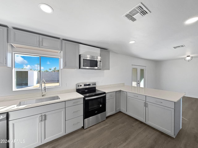 kitchen with dark wood-type flooring, kitchen peninsula, sink, gray cabinetry, and appliances with stainless steel finishes