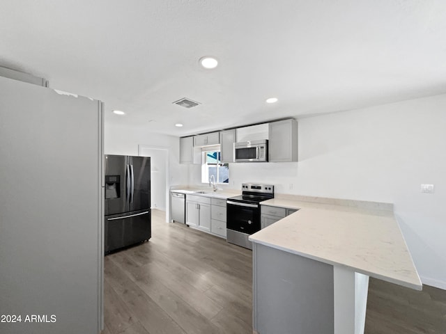 kitchen featuring kitchen peninsula, hardwood / wood-style flooring, a breakfast bar area, gray cabinets, and appliances with stainless steel finishes