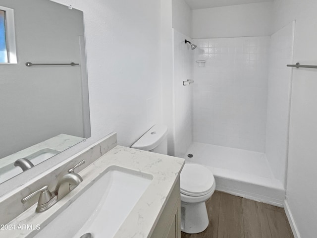 bathroom with wood-type flooring, vanity, toilet, and tiled shower