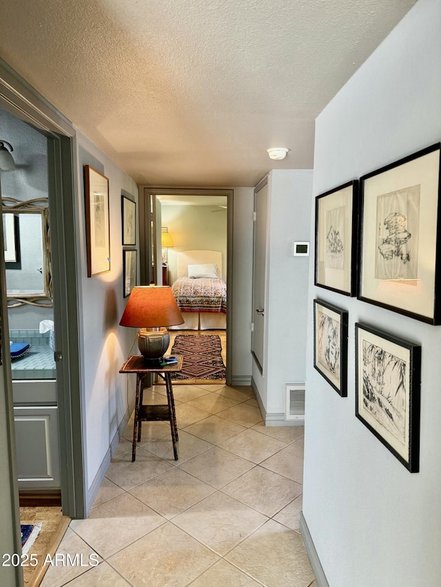 hallway with light tile patterned floors, visible vents, baseboards, and a textured ceiling