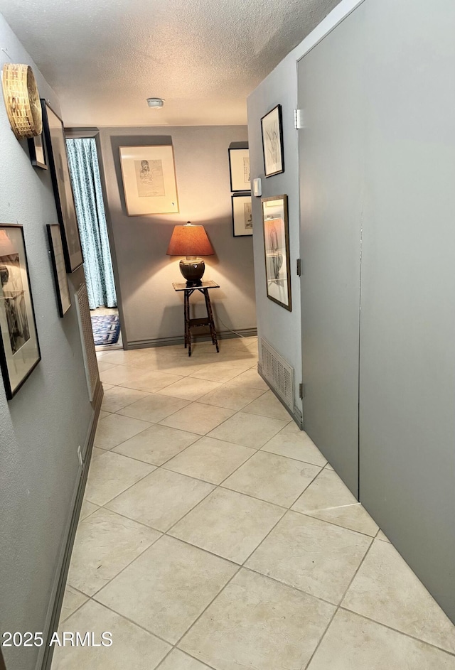 hall with light tile patterned floors, baseboards, visible vents, and a textured ceiling