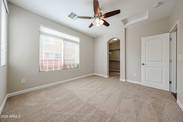 unfurnished bedroom with baseboards, attic access, arched walkways, a spacious closet, and carpet flooring