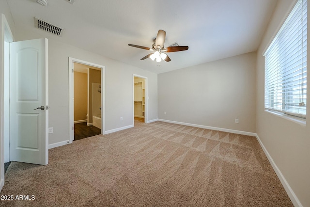 unfurnished bedroom featuring visible vents, a walk in closet, baseboards, carpet, and ensuite bath