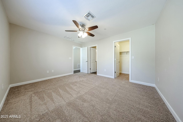 unfurnished bedroom featuring visible vents, a walk in closet, ceiling fan, baseboards, and carpet