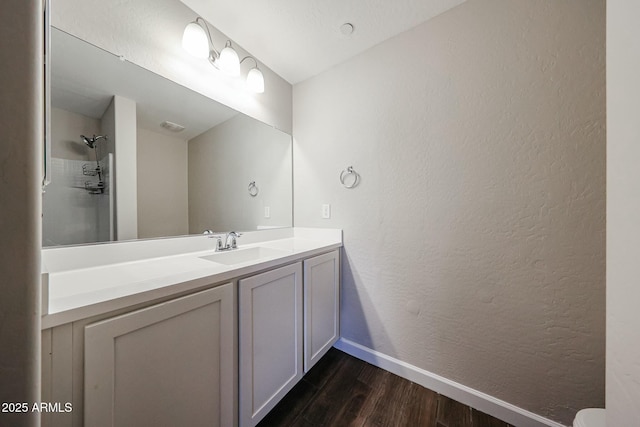 bathroom with baseboards, wood finished floors, a textured wall, vanity, and a shower