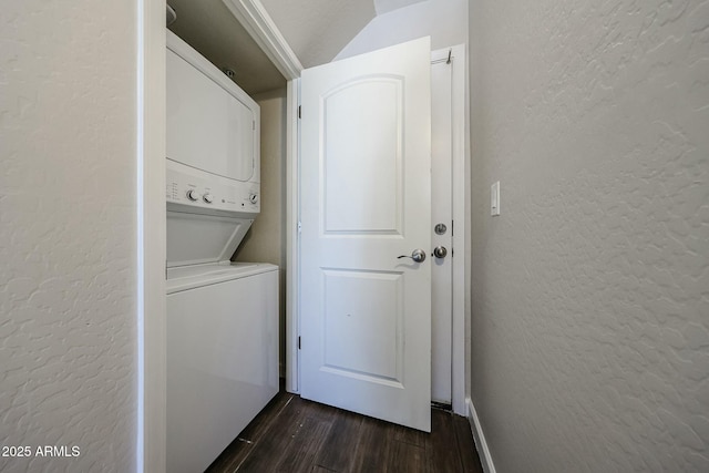 clothes washing area with dark wood-style flooring, stacked washing maching and dryer, laundry area, and a textured wall