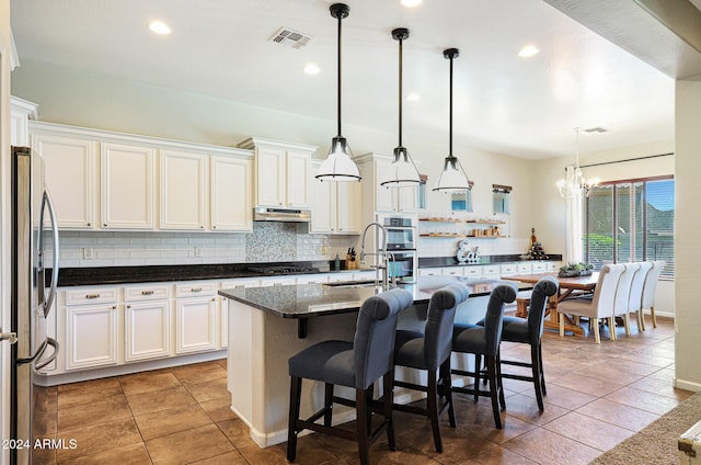 kitchen featuring hanging light fixtures, a kitchen island with sink, white cabinets, appliances with stainless steel finishes, and sink