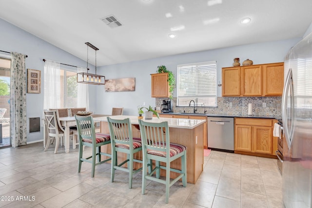 kitchen featuring appliances with stainless steel finishes, a sink, a center island, backsplash, and vaulted ceiling