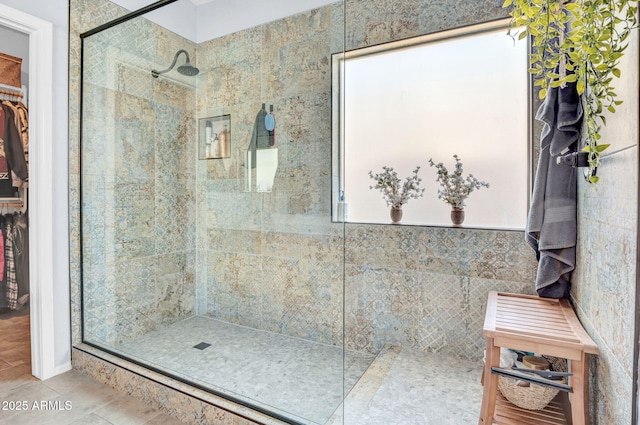full bath featuring tile patterned flooring, a spacious closet, and tiled shower