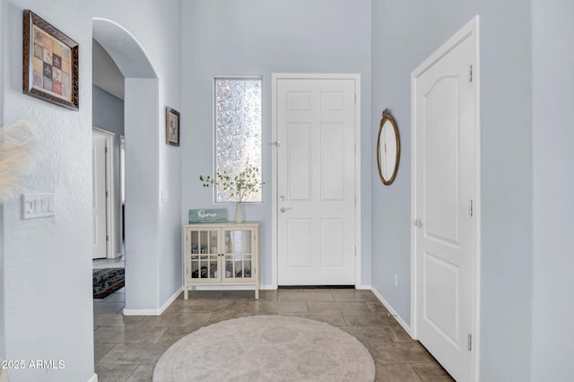 entrance foyer featuring baseboards, arched walkways, and a towering ceiling