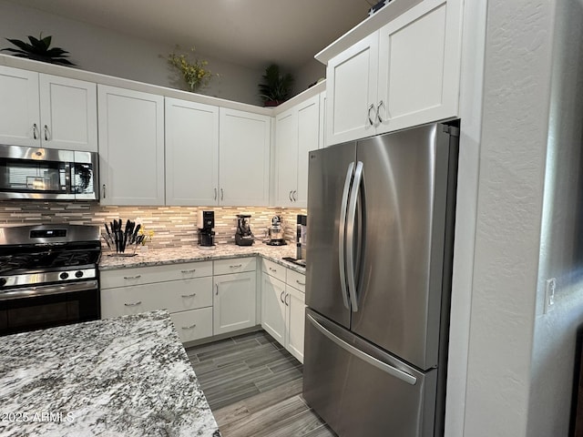 kitchen with appliances with stainless steel finishes, backsplash, white cabinets, and light stone counters