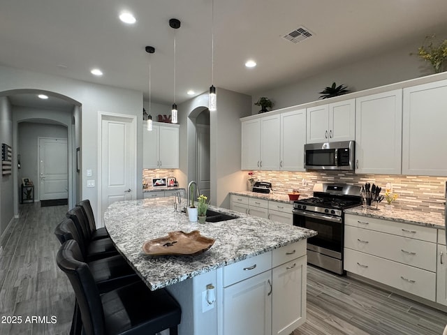 kitchen with sink, stainless steel appliances, an island with sink, and white cabinets