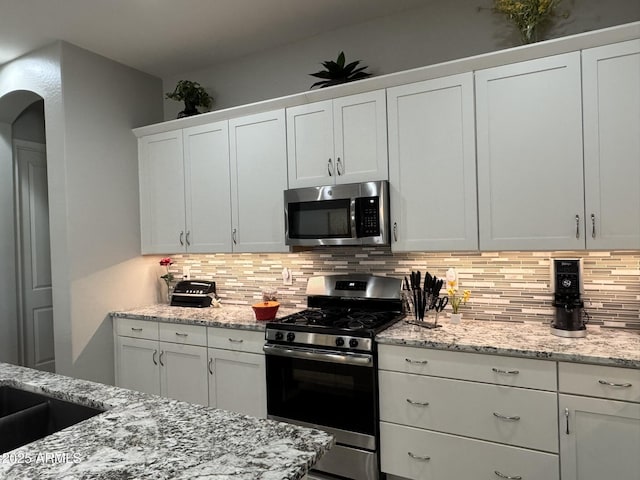 kitchen featuring white cabinetry, stainless steel appliances, light stone counters, and decorative backsplash