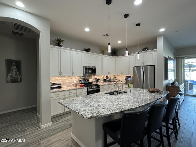 kitchen featuring decorative light fixtures, sink, white cabinets, stainless steel appliances, and a center island with sink