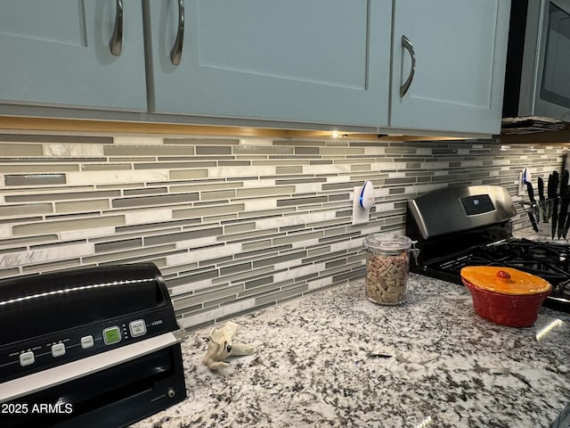 details featuring light stone counters, backsplash, blue cabinetry, and gas stove