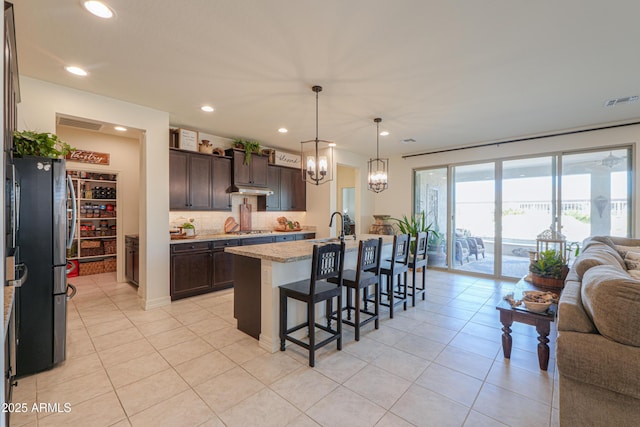 kitchen featuring a breakfast bar area, appliances with stainless steel finishes, dark brown cabinets, light stone countertops, and a center island with sink