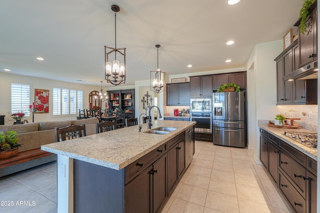 kitchen featuring dark brown cabinetry, sink, an inviting chandelier, appliances with stainless steel finishes, and an island with sink