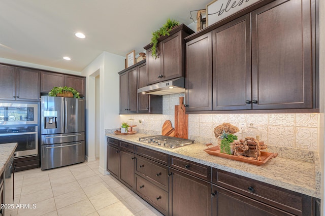 kitchen featuring backsplash, light tile patterned floors, dark brown cabinetry, stainless steel appliances, and light stone countertops