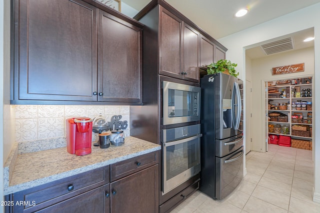 kitchen featuring backsplash, light tile patterned floors, dark brown cabinetry, stainless steel appliances, and light stone countertops