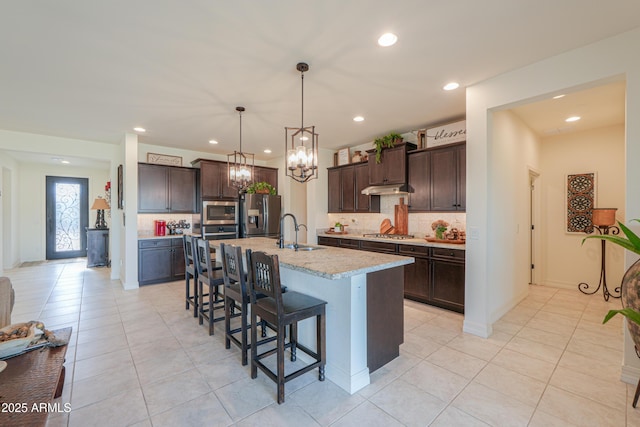 kitchen featuring a breakfast bar, sink, dark brown cabinets, stainless steel appliances, and a kitchen island with sink