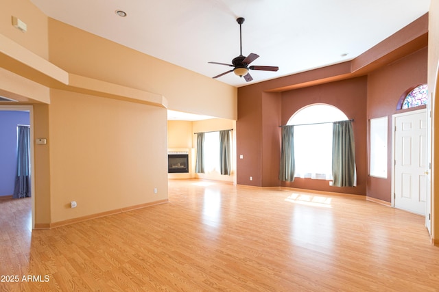 4484 Desert Springs Trl, Sierra Vista, AZ 85635 - unfurnished living room with a ceiling fan, light wood-type flooring, a glass covered fireplace, a high ceiling, and baseboards