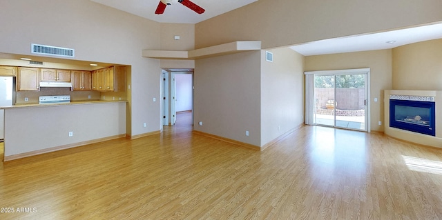 4484 Desert Springs Trl, Sierra Vista, AZ 85635 - unfurnished living room featuring light wood-style flooring, ceiling fan, baseboards, a glass covered fireplace, and a towering ceiling