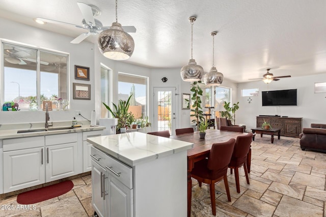 4331 E Redwood Ln, Phoenix, AZ 85048 - kitchen with ceiling fan, stone tile flooring, hanging light fixtures, white cabinetry, and open floor plan