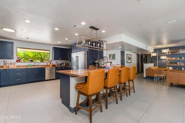 7102 E Kalil Dr, Scottsdale, AZ 85254 - kitchen with wooden counters, stainless steel appliances, backsplash, a breakfast bar area, and blue cabinets