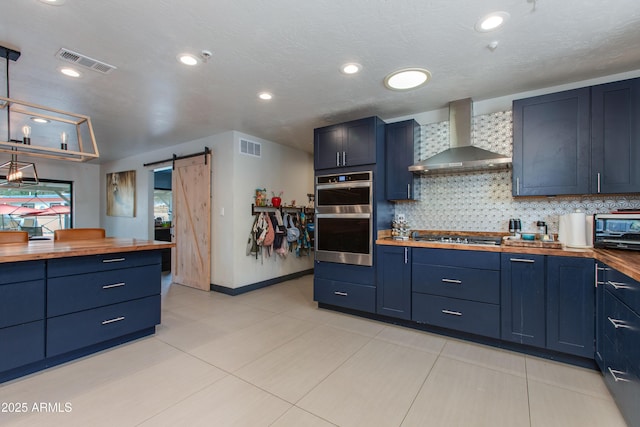 7102 E Kalil Dr, Scottsdale, AZ 85254 - kitchen featuring butcher block countertops, wall chimney range hood, stainless steel appliances, blue cabinets, and a barn door