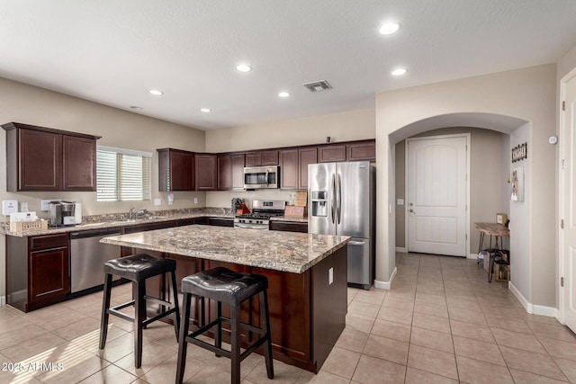 kitchen featuring arched walkways, dark brown cabinetry, a kitchen island, visible vents, and appliances with stainless steel finishes